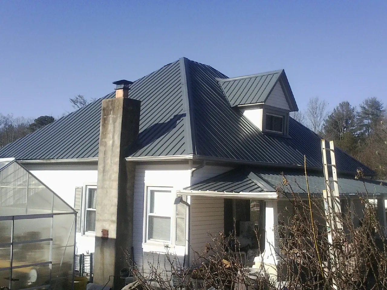 Dark blue standing seam metal roof on a white farmhouse with dormer — Slate & Tile Roof Repair by Roofing Brothers in Sale Creek