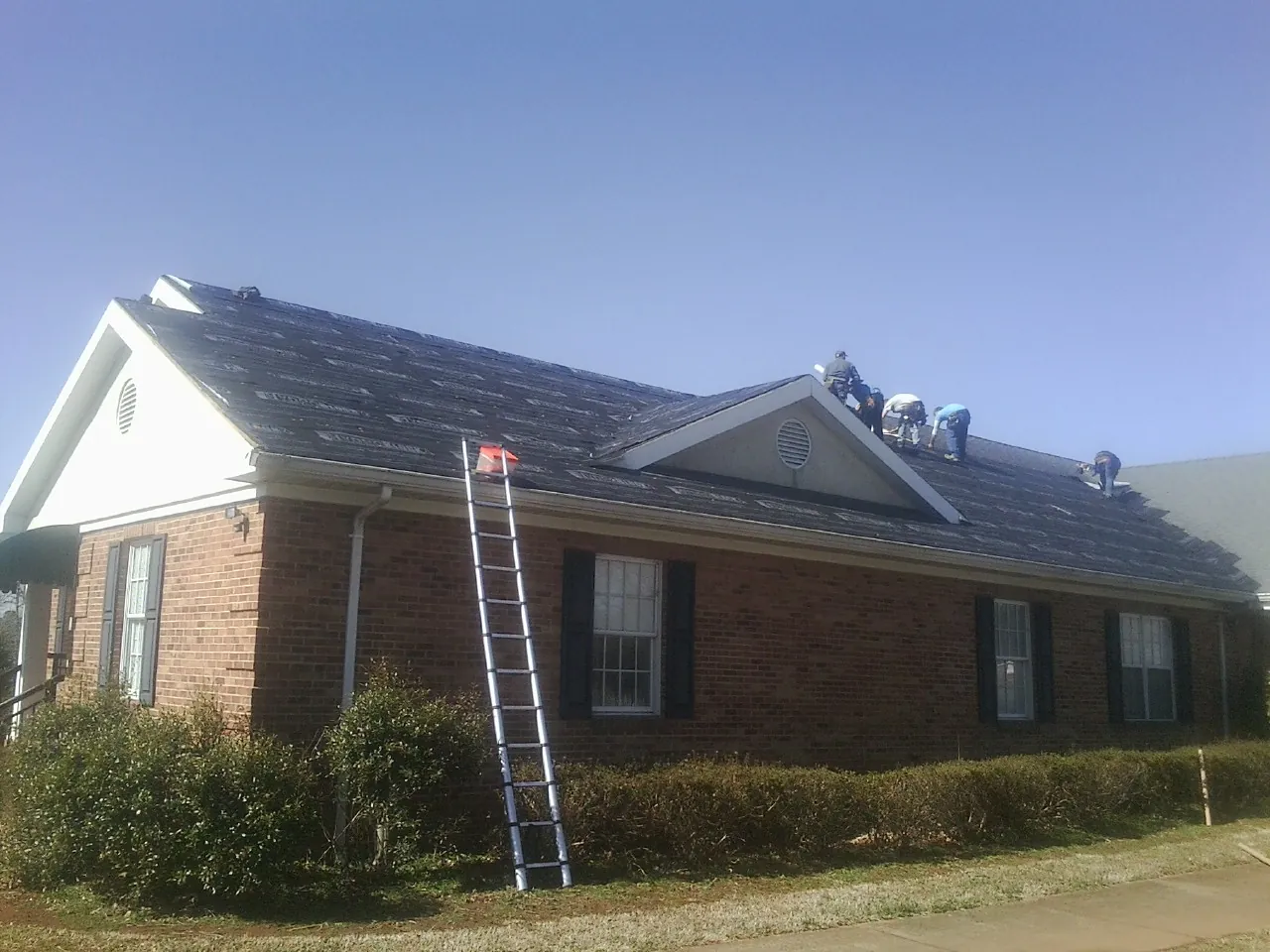 Crew tearing shingles off a brick ranch roof with a ladder set — Metal Roof Repair work by our crew in Sale Creek