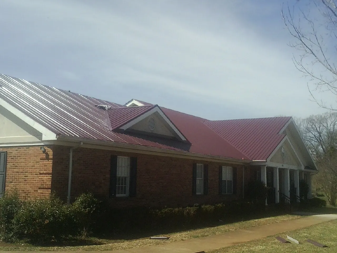 Red metal roof with gabled entries on a long brick building, from a Hail Damage Roof Repair job in Sale Creek