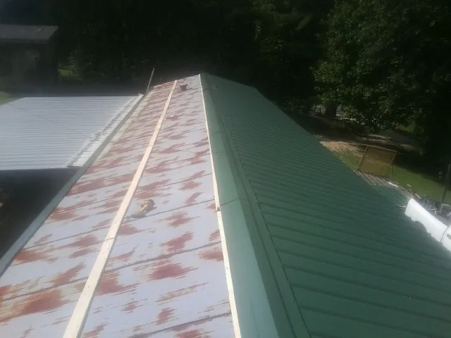 Old rusted panels beside newly installed green metal roofing — Wind Damage Roof Repair by Roofing Brothers in Sale Creek