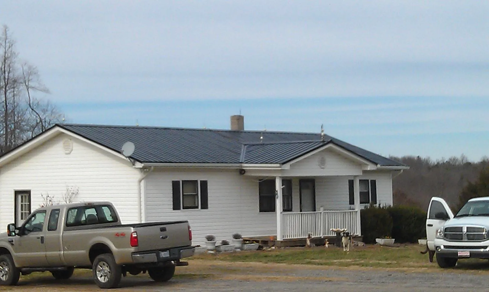 Finished dark metal roof on a white ranch home with work trucks parked in Sale Creek