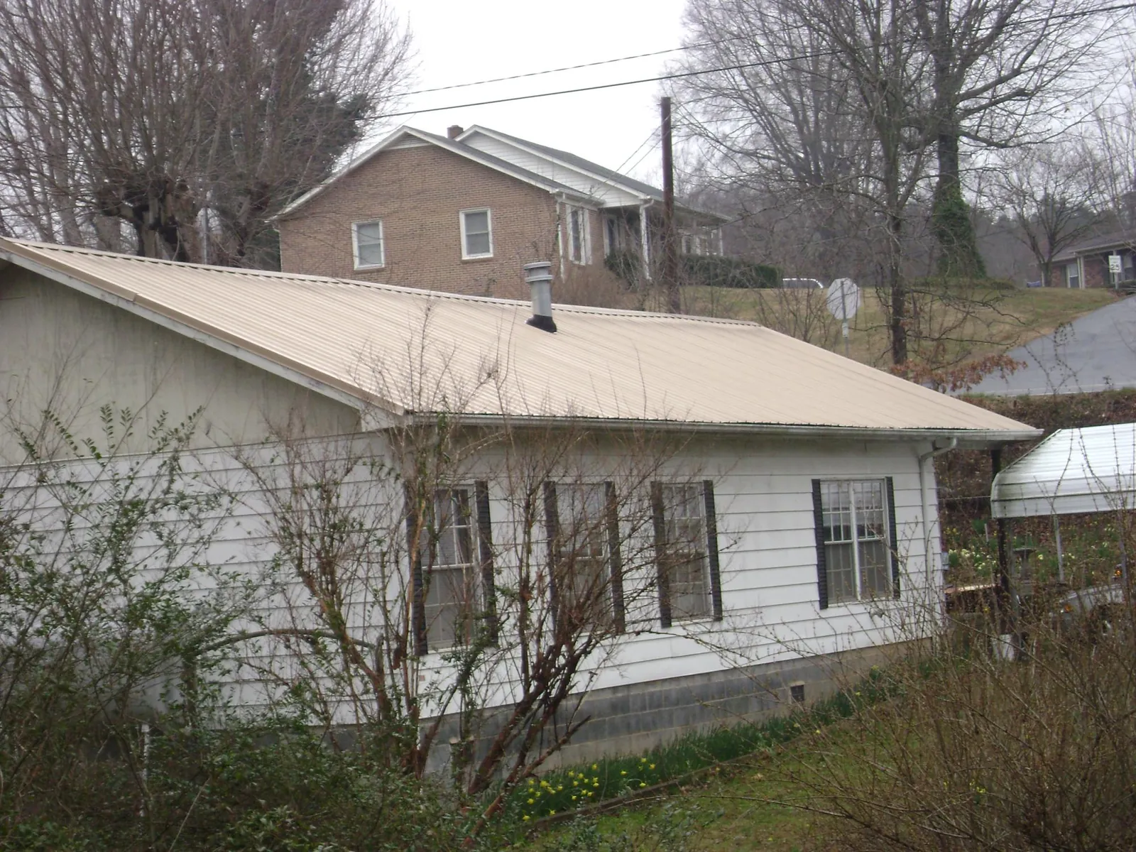 Tan metal roof on a white sided house set into a hillside — Commercial Roofing by Roofing Brothers in Sale Creek
