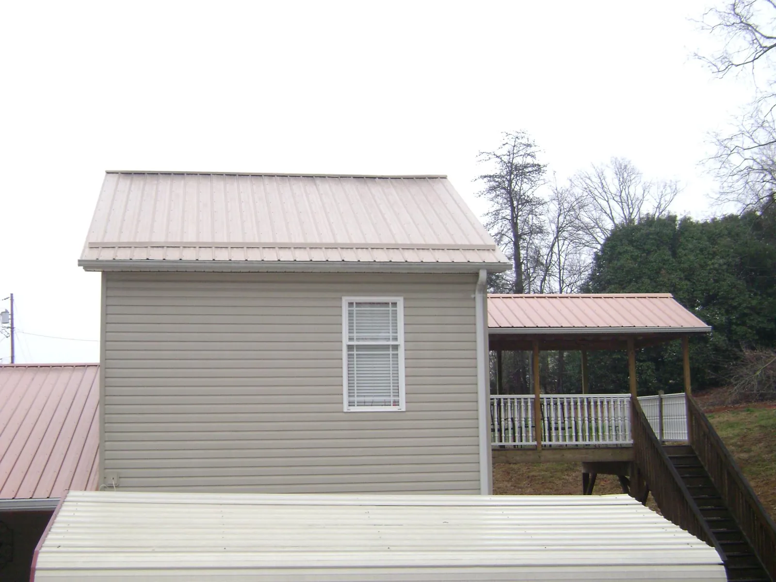 Tan metal roofs on a two story addition and attached porch, from a Roof Replacement job in Sale Creek